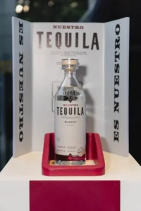 Botella de Nuestro Tequila Blanco 100% agave presentada en exhibición institucional con sello Hecho en México.
