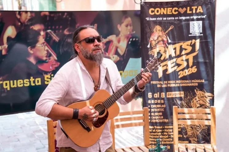 Damián Martínez interpreta una pieza musical durante una presentación relacionada con el Bats'i Fest 2026, frente al cartel oficial del festival y como símbolo de su legado cultural.