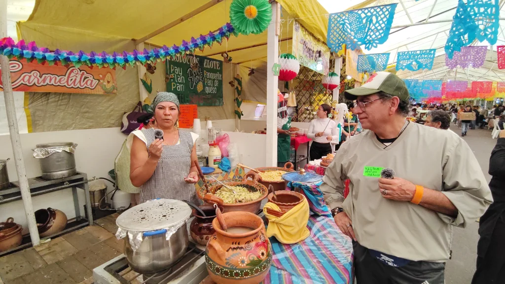 Expositora de la Feria del Elote 2026 en San Juan Ixtayopan ofreciendo platillos tradicionales elaborados con maíz criollo en un ambiente festivo y comunitario.