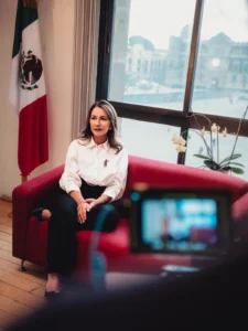 Leonor Otegui durante entrevista en Ciudad de México, con la bandera nacional al fondo, hablando sobre su propuesta de deducción fiscal para la vacuna contra el VPH.