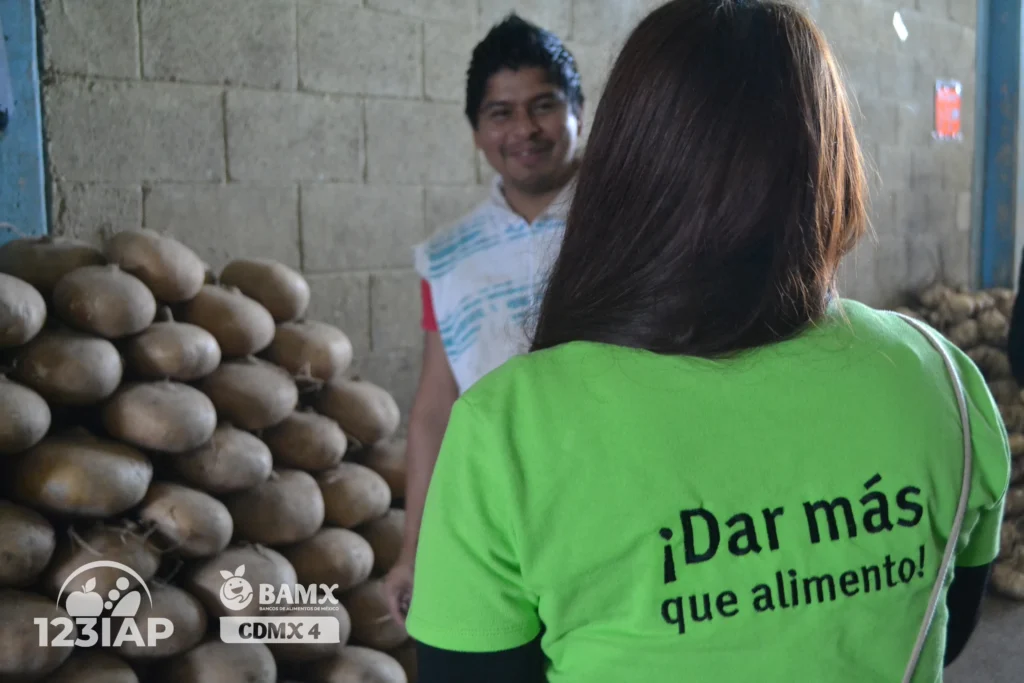 Voluntarios de 123 IAP en almacén de alimentos con mensaje “Dar más que alimento”.