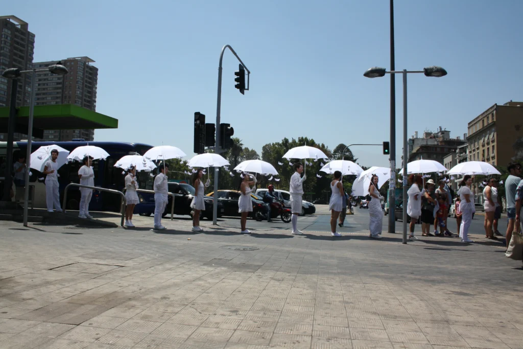 Intervención escénica Lluvia de Palabras en el 33 FITU, con performers vestidos de blanco y paraguas en espacio público del Centro Cultural Universitario.