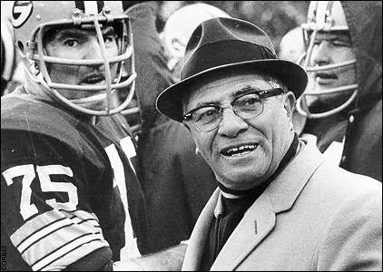 Fotografía histórica de Vince Lombardi durante un partido de futbol americano profesional acompañado por jugadores en la banca de la NFL.